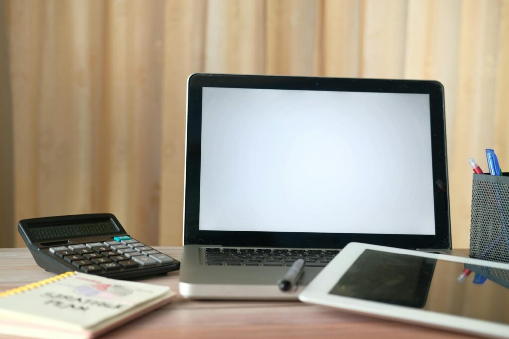 A tidy home-office desk with a laptop showing a portfolio spreadsheet and a notebook beside it.