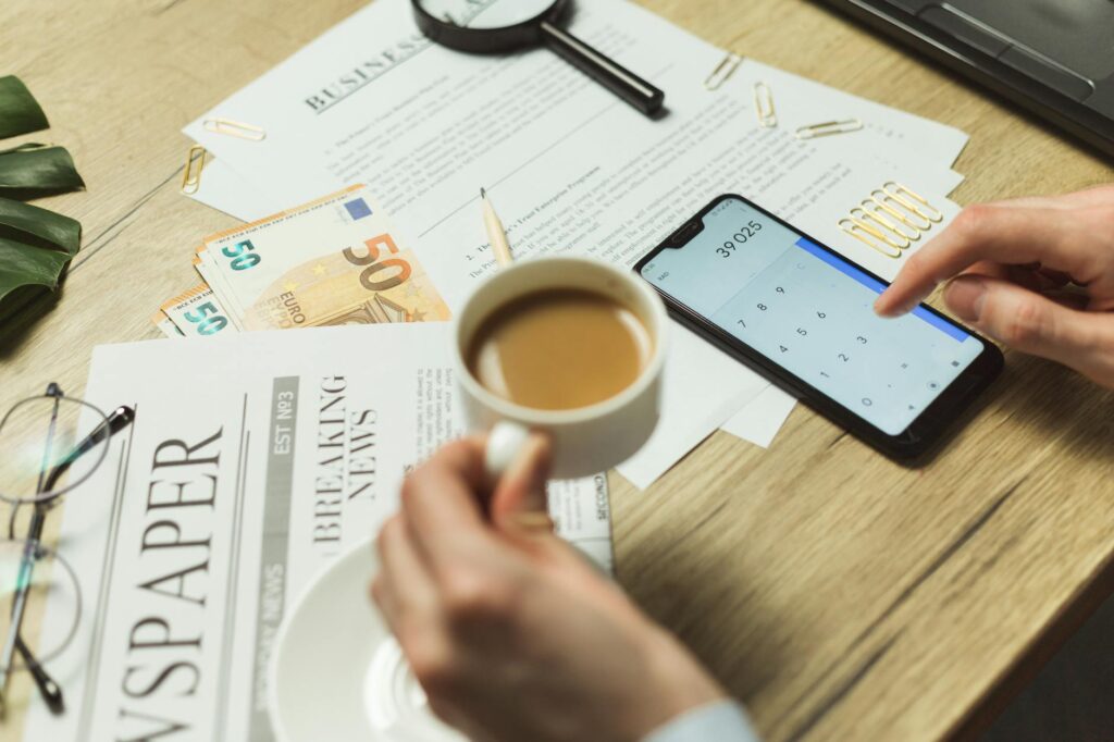 A desk with investment paperwork, a calculator, and a smartphone next to a notebook