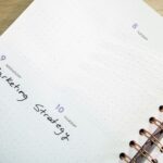 A person writing stock, bond, and cash allocation targets on a notepad next to account paperwork.