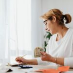 A tidy desk with a calculator, calendar, notebook, and papers showing household savings goals.