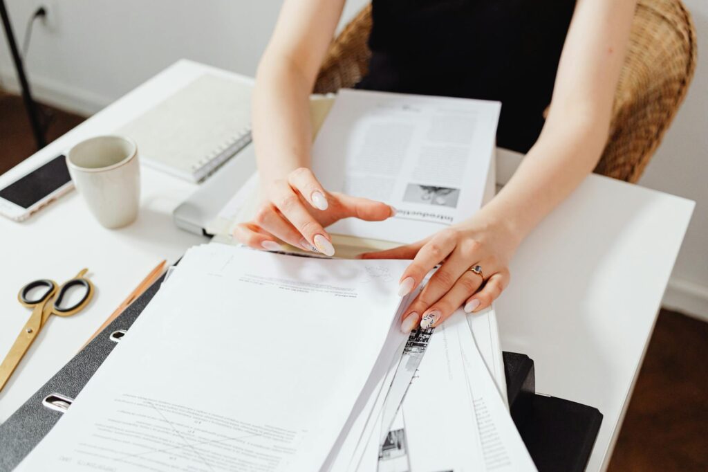 Hands organizing investment account paperwork next to a laptop on a desk