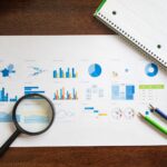 Printed investment statements, a calculator, and a notebook on a home desk