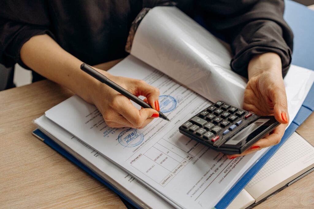A person reviewing year-end financial records with a calculator and paper forms on a desk.